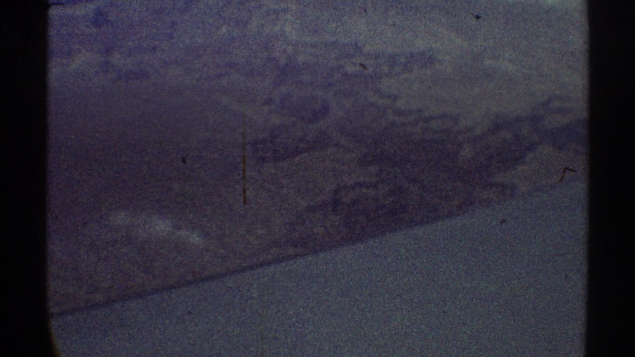 Grainy aerial view through a dark airplane window over hazy rugged terrain.
