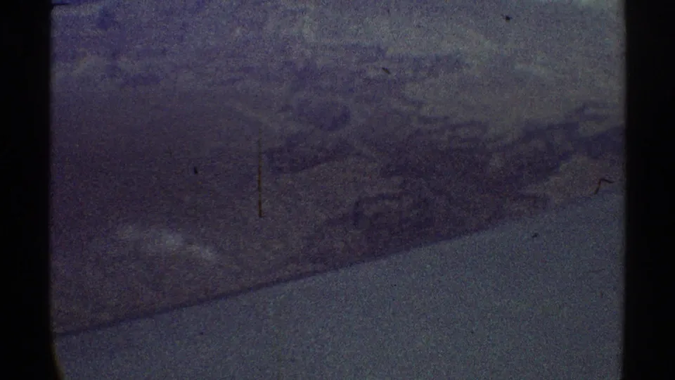 1969 8mm home-movie frame looking from an airplane window toward muted mountain or desert terrain near the Los Angeles-area context.