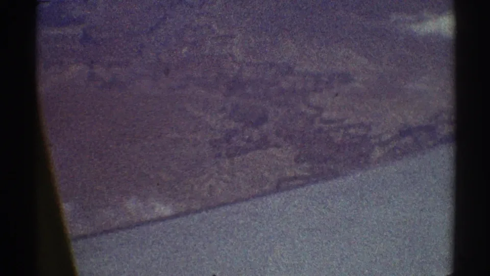 1969 8mm frame showing a passenger-window aerial view of dry, rugged landforms with visible film borders and color drift.
