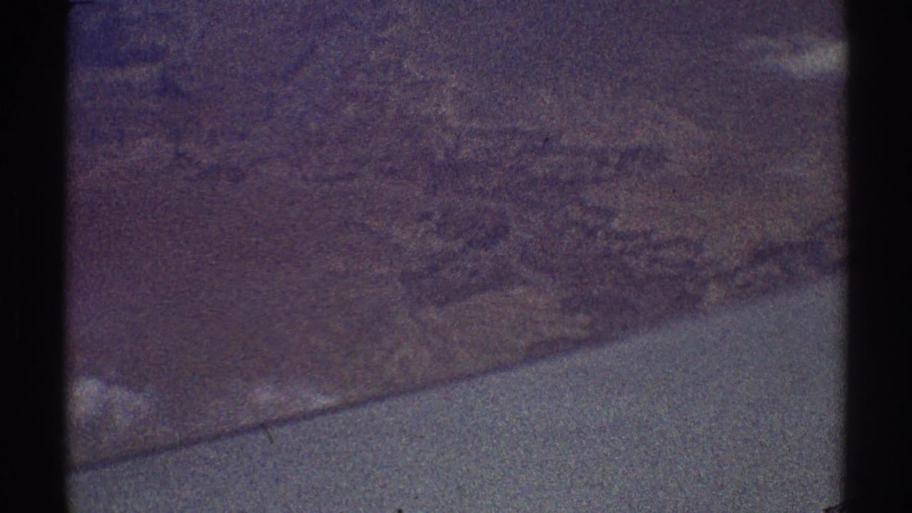 Grainy aerial view of textured land or shoreline through dark frame borders.