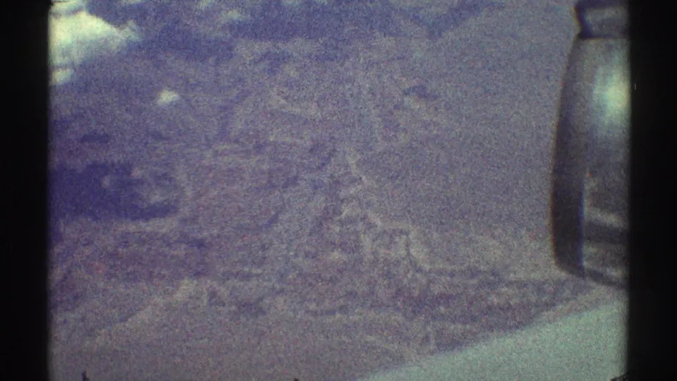 1969 home-movie aerial frame showing blurred land or water texture, dark borders, and a bright patch near the left edge.