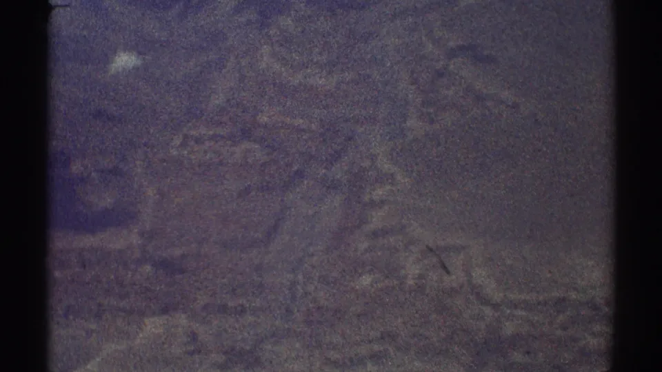 Late-1960s 8mm frame of an indistinct aerial landscape, with heavy grain, muted color, and dark frame edges.