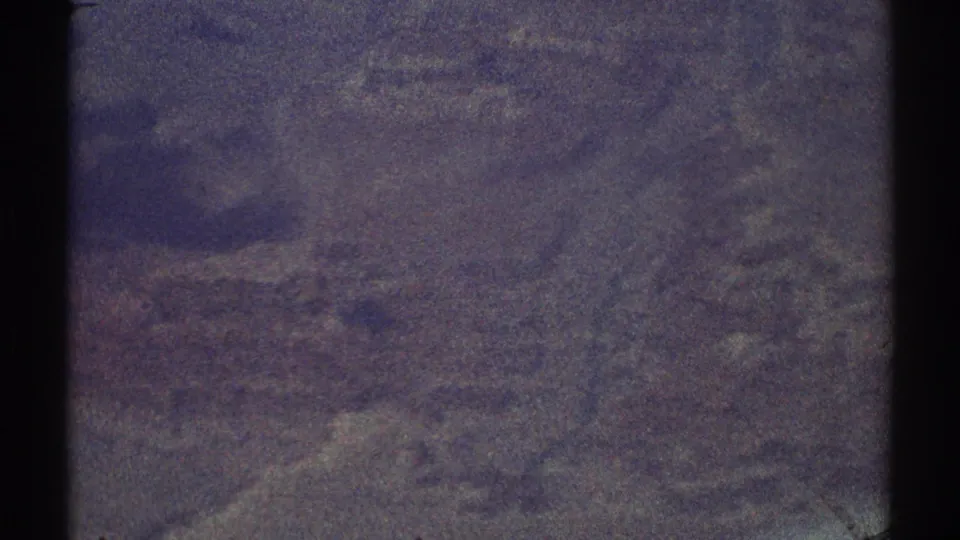 Purple-shifted 1969 8mm aerial frame showing indistinct terrain from high above.