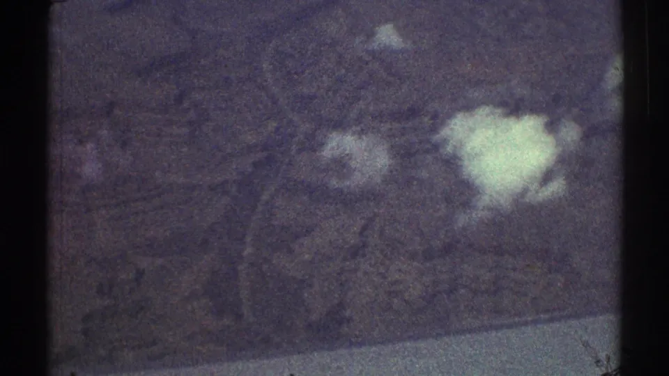 1969 8mm aerial view of textured ground and scattered white clouds, with soft focus and visible film grain.