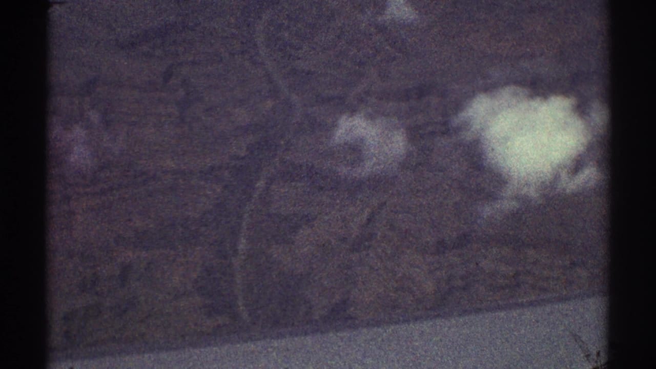 Grainy aerial view of hills, pale water edge, and white clouds through film frame borders.
