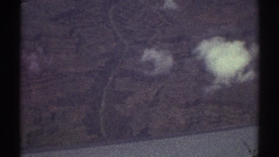 1969 8mm Los Angeles-area aerial view over rugged hills with white clouds and a pale water or valley edge below.
