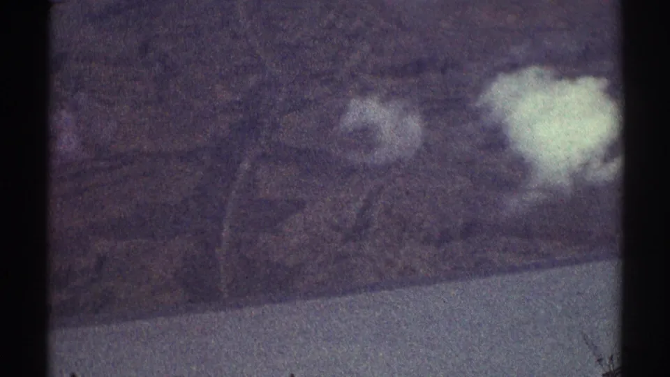 Vintage 8mm aerial frame showing Los Angeles-area hills, bright cloud patches, and a pale lower landscape edge.