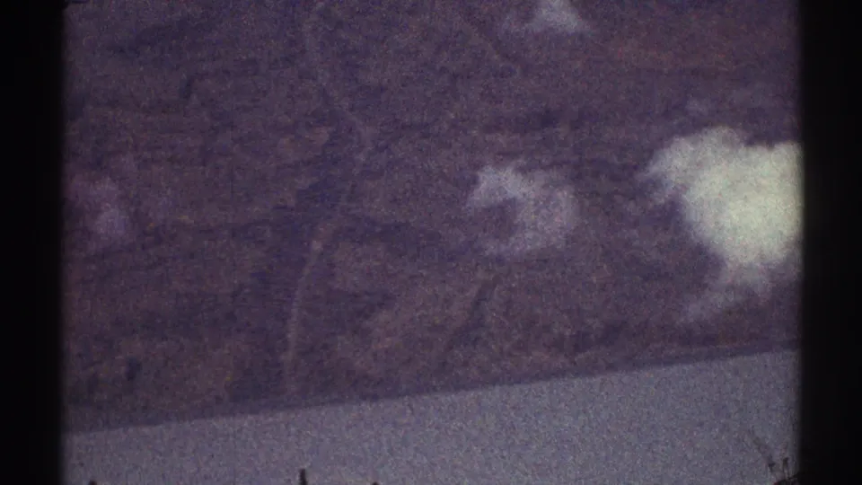 1969 home-movie aerial view over rugged Los Angeles-area terrain, with soft white clouds and visible 8mm gate edges.