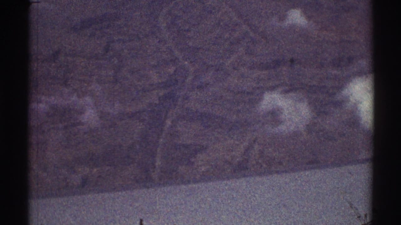 Grainy aerial view of faint terrain, pale road lines, and dark film borders.