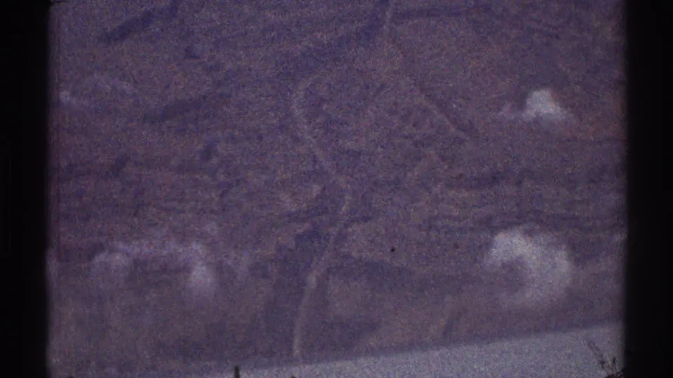Purple-tinted 8mm view over indistinct Los Angeles-area terrain, with faint roads or structure outlines visible through grain.
