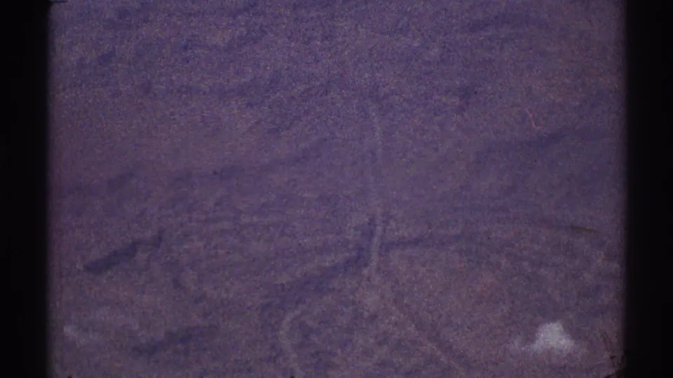 Low-contrast 1969 8mm aerial frame with indistinct terrain, visible scratches, and a strong purple film cast.