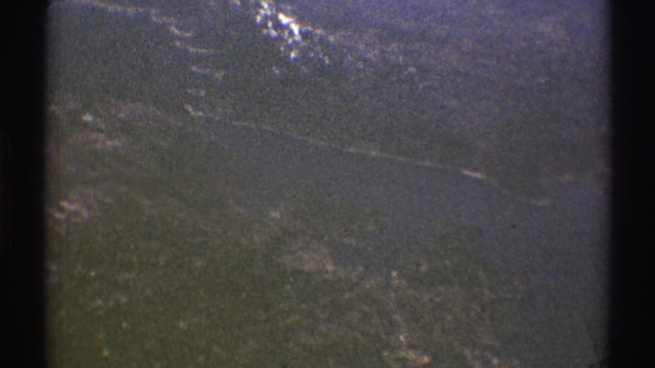 Hazy mountain slope with patches of snow seen through dark aircraft-window edges.