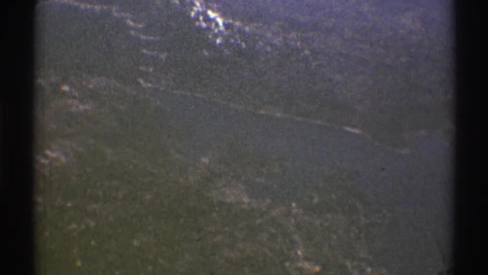 1969 8mm helicopter view near Los Angeles, showing a hazy forested mountain slope with small snow patches and dark window framing.