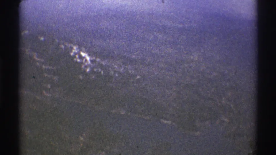 1969 8mm aerial view near Los Angeles with snow-streaked mountain ridges, haze, and a dark helicopter-window divider.