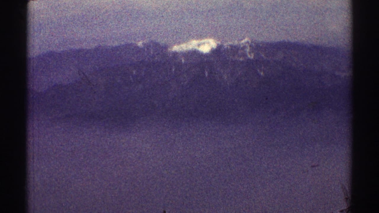 Distant snow-covered mountain peak above a dark ridge under a hazy sky.