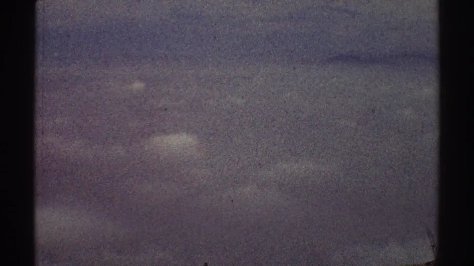 1969 home-movie frame showing hazy sky through dark airplane window dividers above Los Angeles.