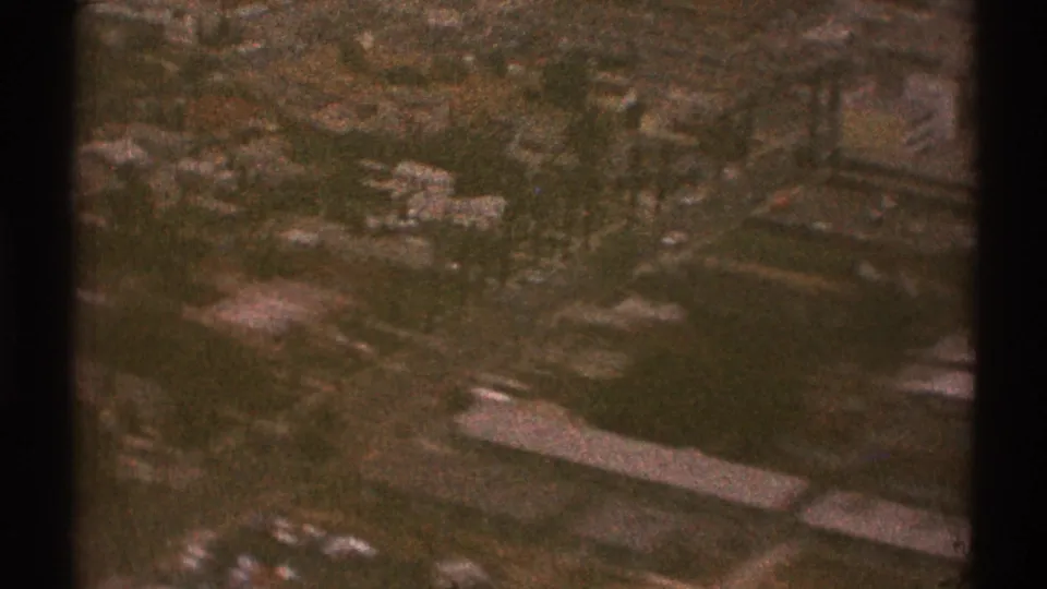Low-light 1969 airplane view over Los Angeles showing roads, buildings, and green areas beneath the window frame.