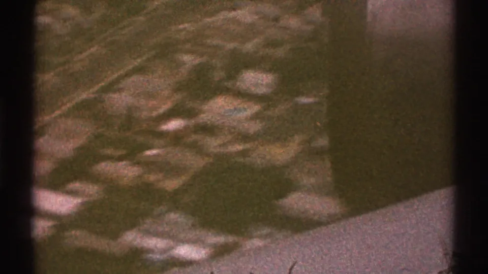 Grainy 1969 Los Angeles aerial view from an airplane, with urban streets, buildings, and open green areas visible below.