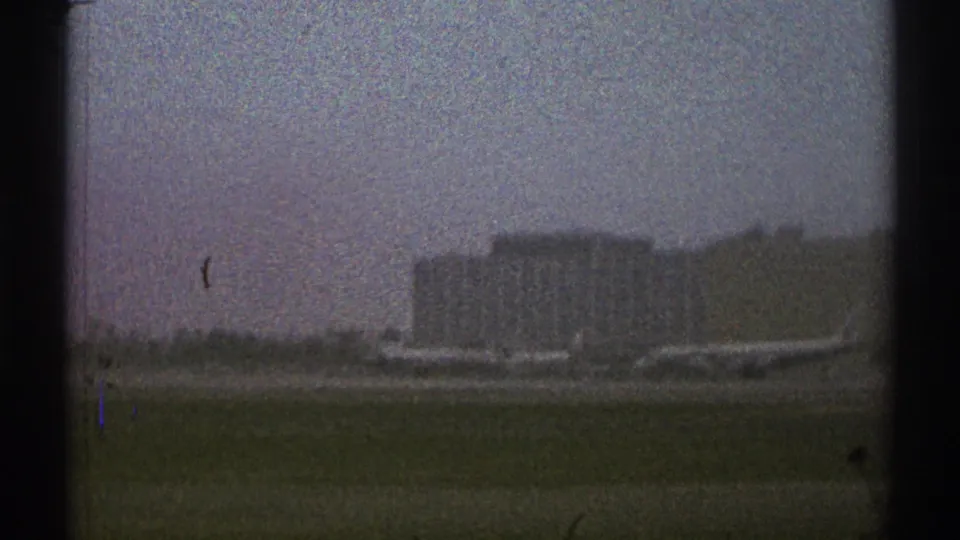 Late-1960s Los Angeles airport runway-side view with grass, parked aircraft, and a distant rectangular airport building.