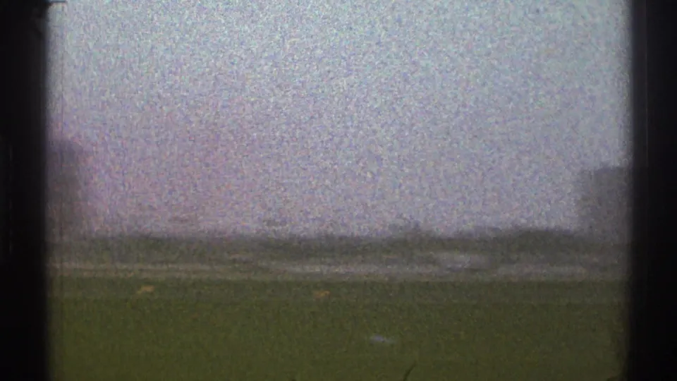 A soft 1969 Los Angeles airport-area view shifts toward open ground, with a distant structure partly visible at the frame edge.