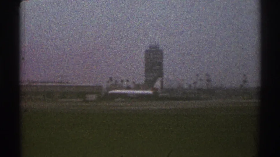 1969 Los Angeles-area airport view with a control tower, low buildings, and an aircraft-like shape on the tarmac under a gray sky.