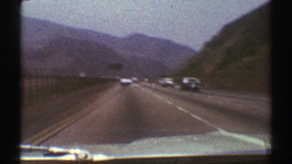 Moving-car view on a Los Angeles-area mountain highway, with traffic in both directions and the car hood visible.