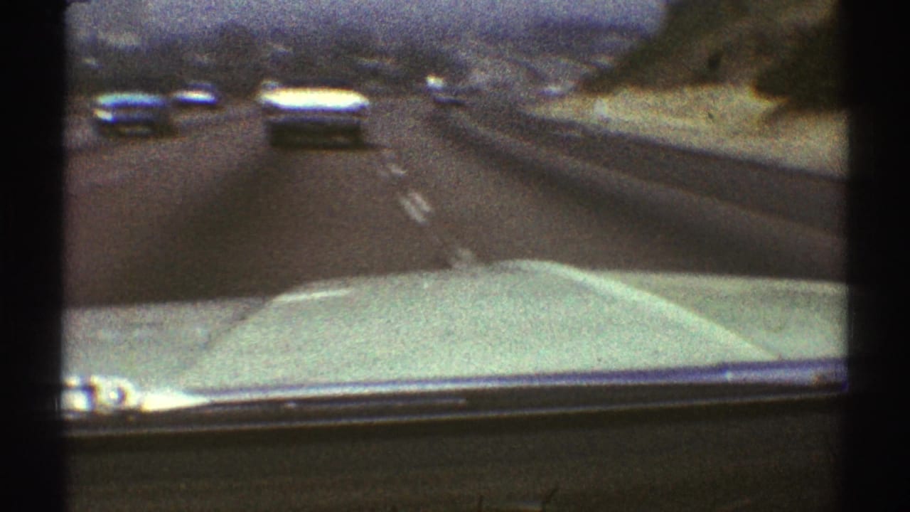 Multi-lane highway seen over a pale car hood with several cars ahead.