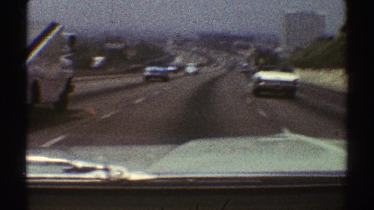 Forward view from a car on a multi-lane highway with traffic, car hood, and hazy skyline.