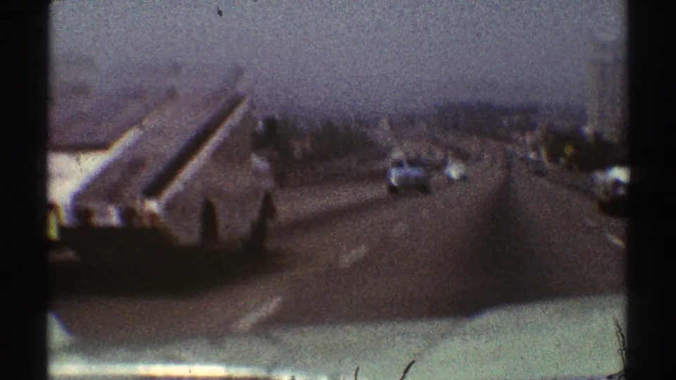 Forward-facing 8mm view on a Los Angeles highway in 1969, showing traffic ahead, road lanes, haze, and dark film borders.