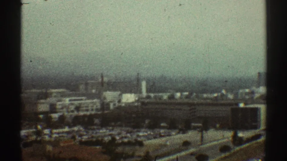 Faded 8mm view of a Los Angeles urban-industrial landscape in 1969, with rooftops, haze, vertical structures, and roadway elements.