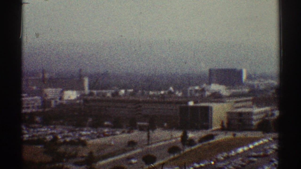 Hazy elevated city view with buildings, roads, parking lots, and dark film-frame edges.