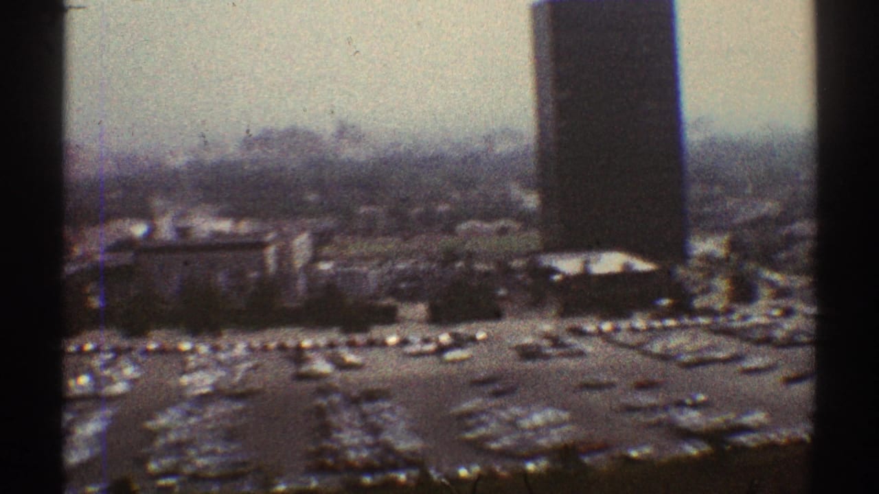 Elevated view of high-rise towers and a crowded parking lot seen through dark vertical obstructions.