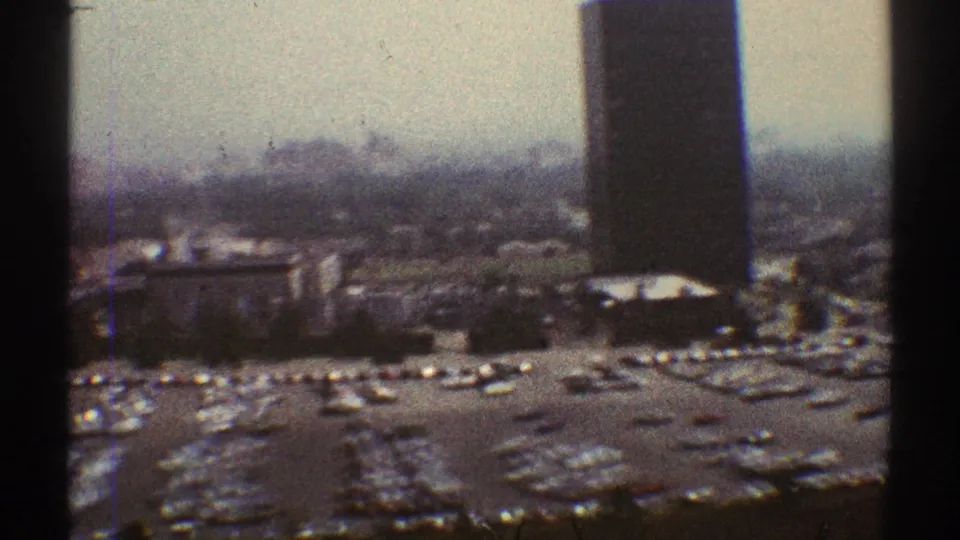 1969 Los Angeles 8mm frame showing tall buildings above a large parking lot filled with cars, partly obscured by dark vertical edges.