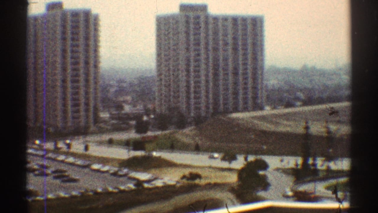 High-angle view of apartment towers, parking lot, lawns, and cars.
