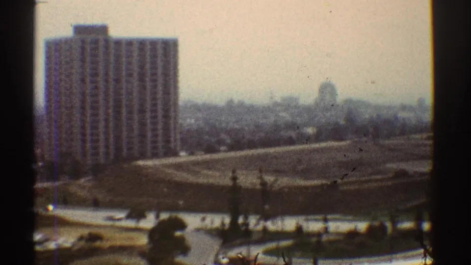 Elevated 1969 Los Angeles view across a high-rise apartment building, open grounds, small cars, and hazy distant buildings.