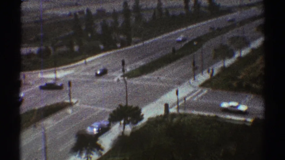 1969 Los Angeles frame showing curving lanes, scattered cars, palm trees, medians, and urban road edges from an elevated viewpoint.