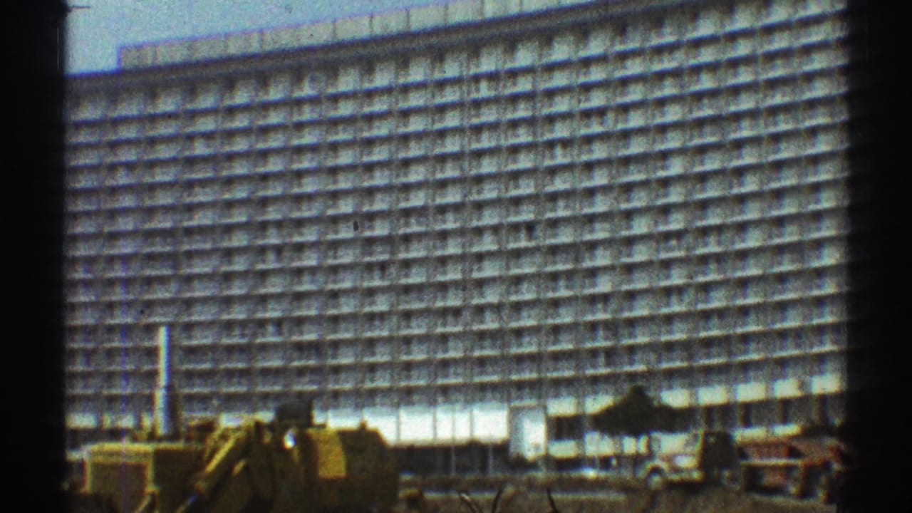 Large white multi-story building with construction equipment in the foreground.