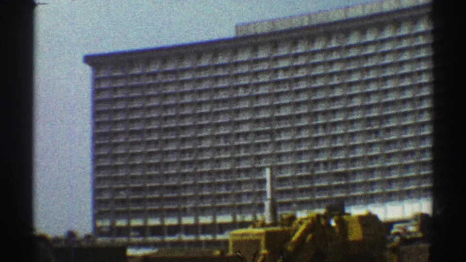 Handheld 8mm frame of a large Los Angeles building, with a yellow excavator and work vehicles at the base.