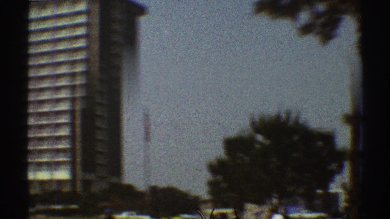 1969 Los Angeles street-level view with a high-rise edge, trees, pale sky, cars, and dark 8mm frame borders.