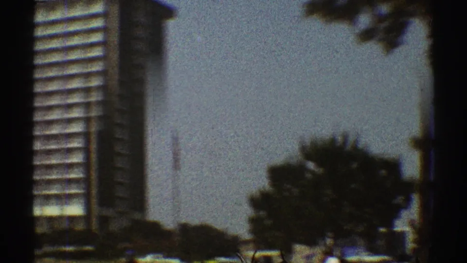 1969 Los Angeles street-level view with a high-rise edge, trees, pale sky, cars, and dark 8mm frame borders.