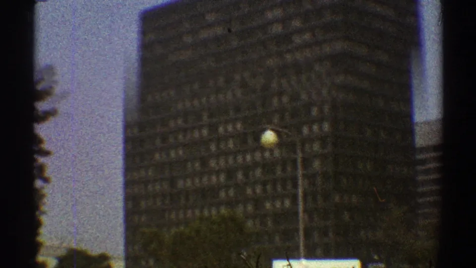 1969 Los Angeles view of a dark high-rise facade with rows of windows, street lights, trees, and visible 8mm frame edges.