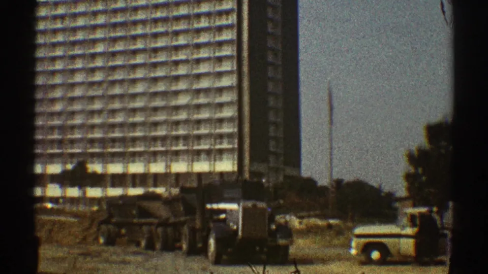 A 1969 Los Angeles street scene shows a dump truck, a light pickup, trees, and a tall modern high-rise in the background.