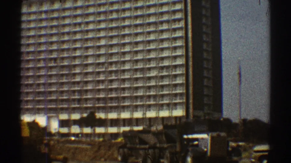 1969 Los Angeles 8mm frame showing the lower portion of a gridded high-rise with construction earth and a small structure in front.