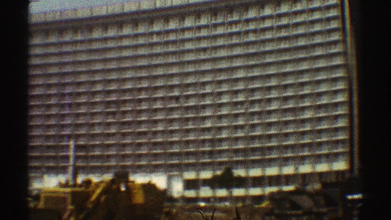 Tall grid-front high-rise seen from street level with machinery at the base.