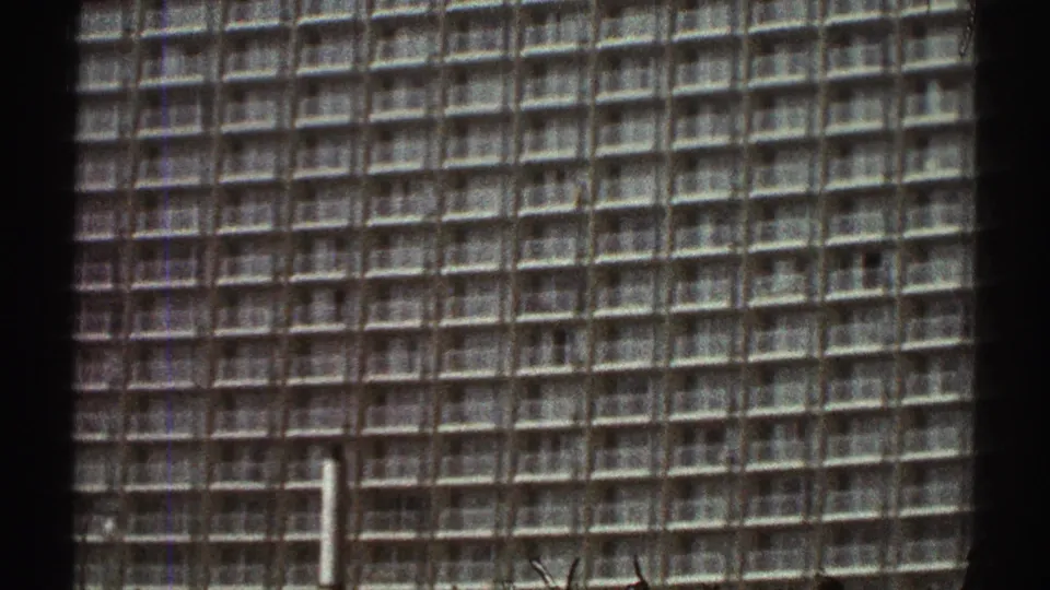 1969 Los Angeles 8mm frame with a large grid-like high-rise facade filling most of the view above the worksite.