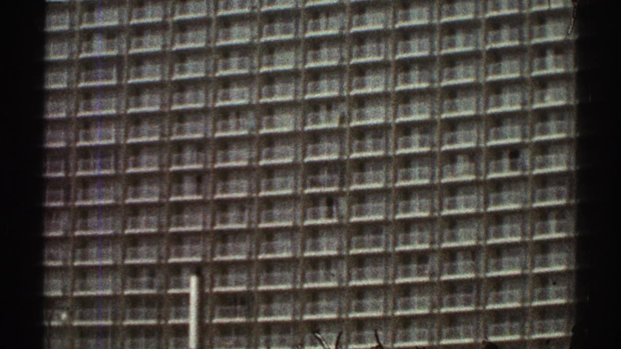 1969 Los Angeles frame showing a tall modern building with a dense grid facade, seen in soft 8mm color with visible film borders.