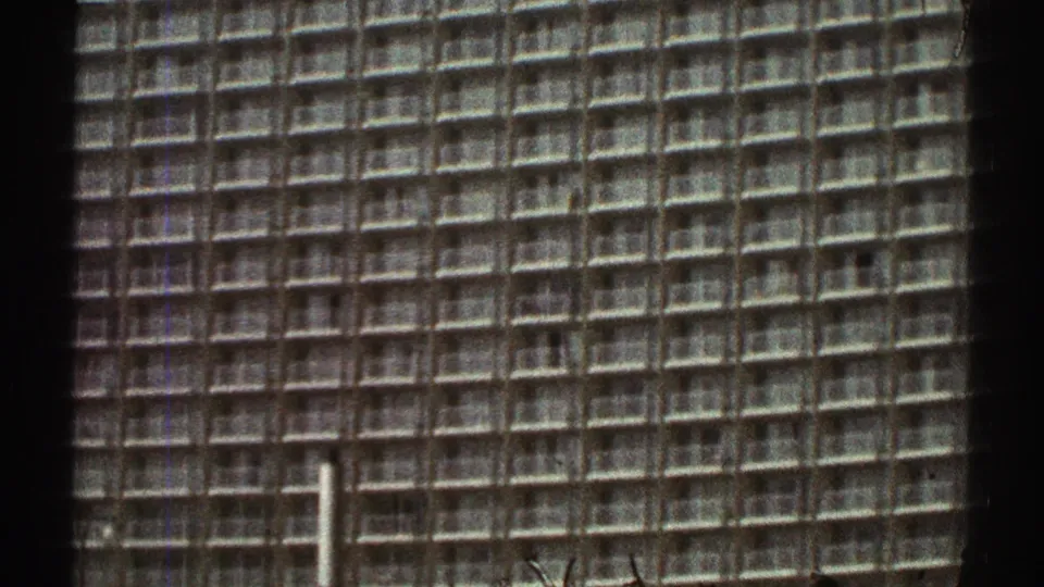 1969 Los Angeles frame showing a tall modern building with a dense grid facade, seen in soft 8mm color with visible film borders.