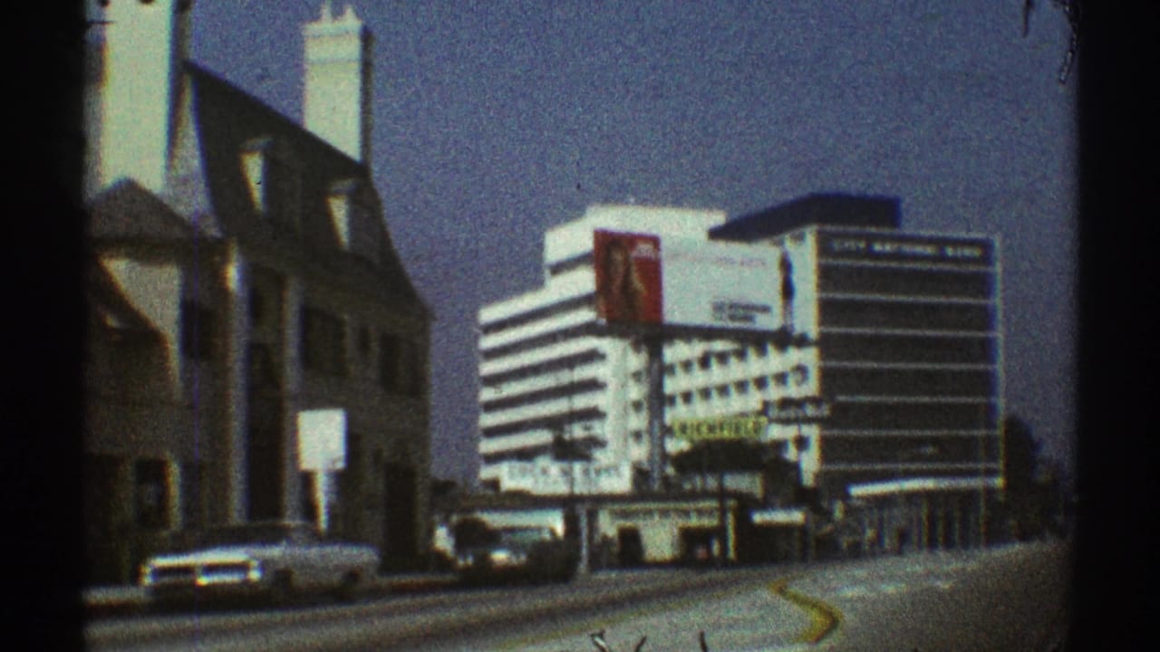 Moving street view with a white sedan, older building, and striped office building ahead.