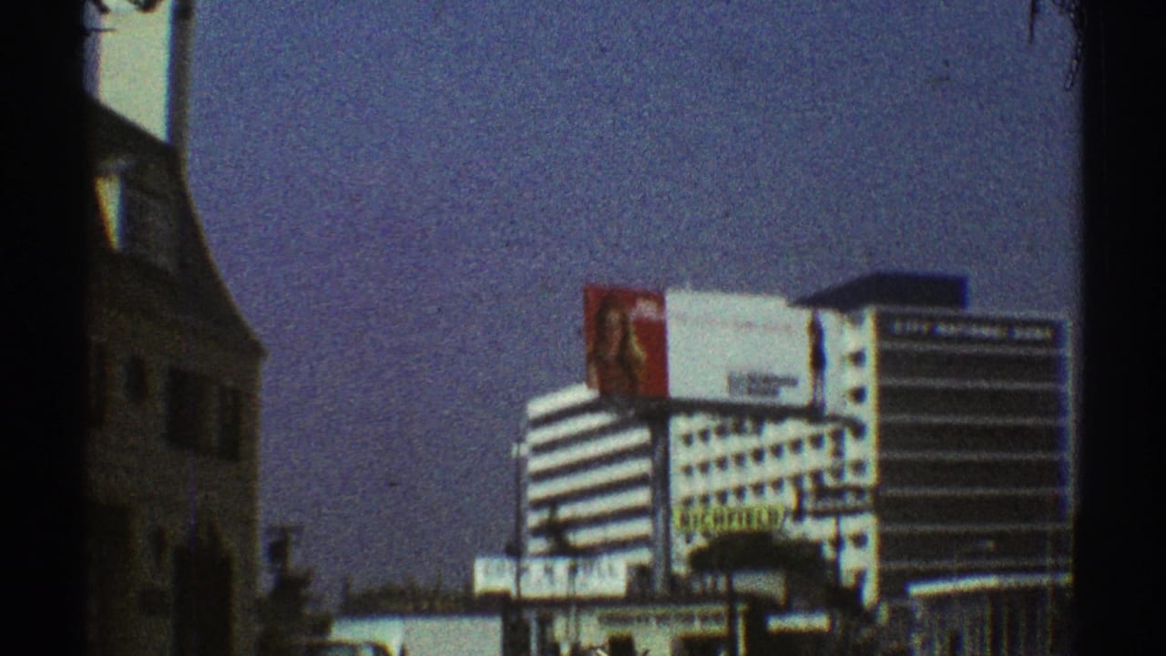 Roadside view of a striped office building with billboard and dark vertical film edge.