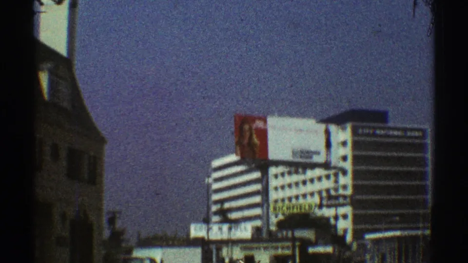 1969 Los Angeles roadside view with a striped commercial building, large billboard, and adjacent older building partly obscured by the film frame edge.